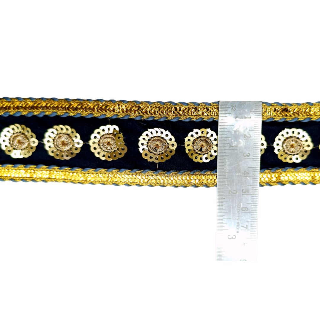Decorative ribbon with gold and black pattern next to a ruler for measurement on a white background