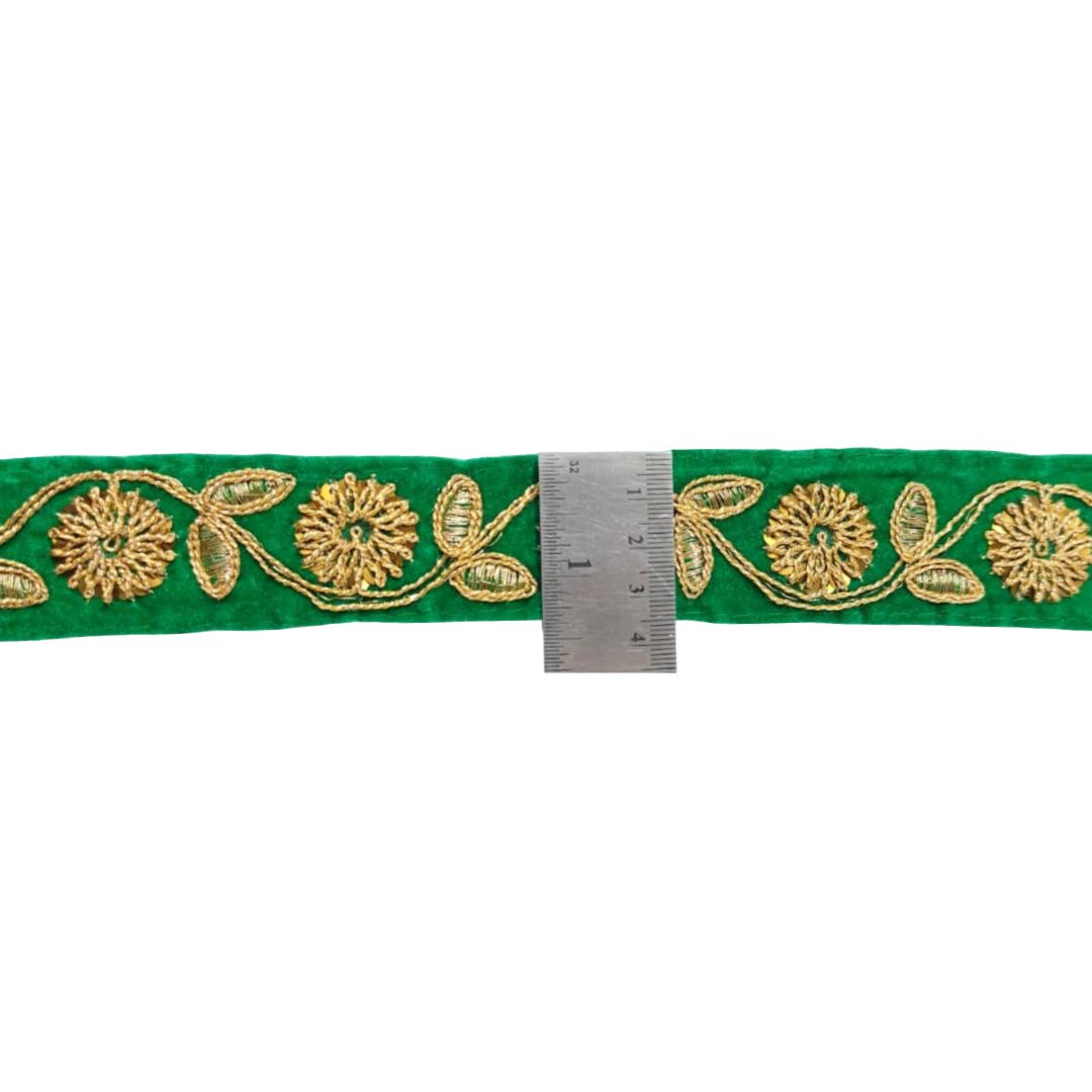 Green ribbon with gold floral embroidery and a ruler for scale on a white background