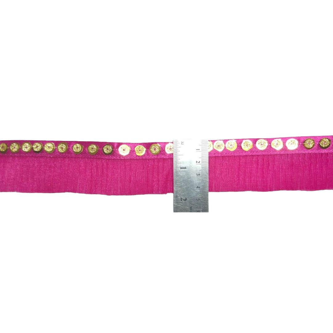 Pink ribbon with decorative gold and white pattern, measured against a ruler on a white background