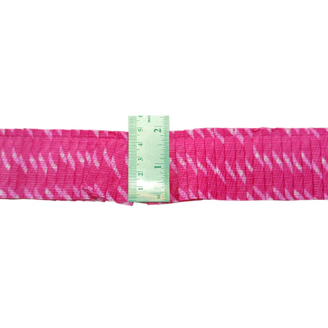 Pink fabric with white patterns and a green measuring tape on a white background