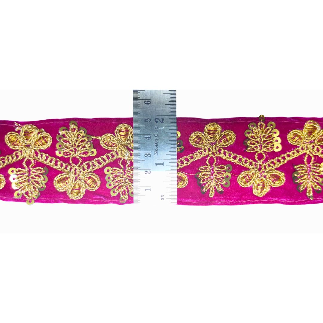 Gold embroidered fabric on a pink background with a ruler for scale.