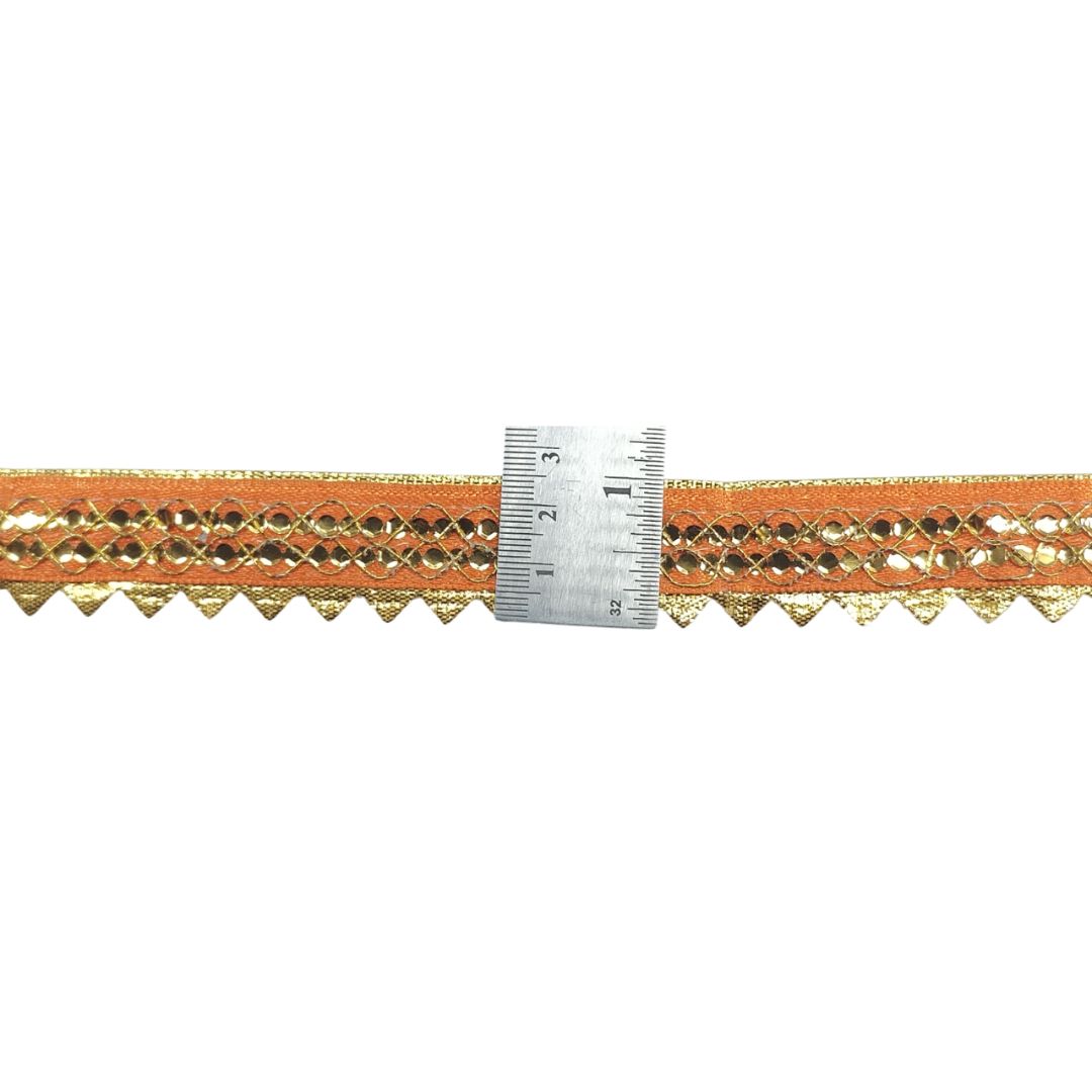 Orange fabric trim with gold pattern and a ruler for scale on a white background