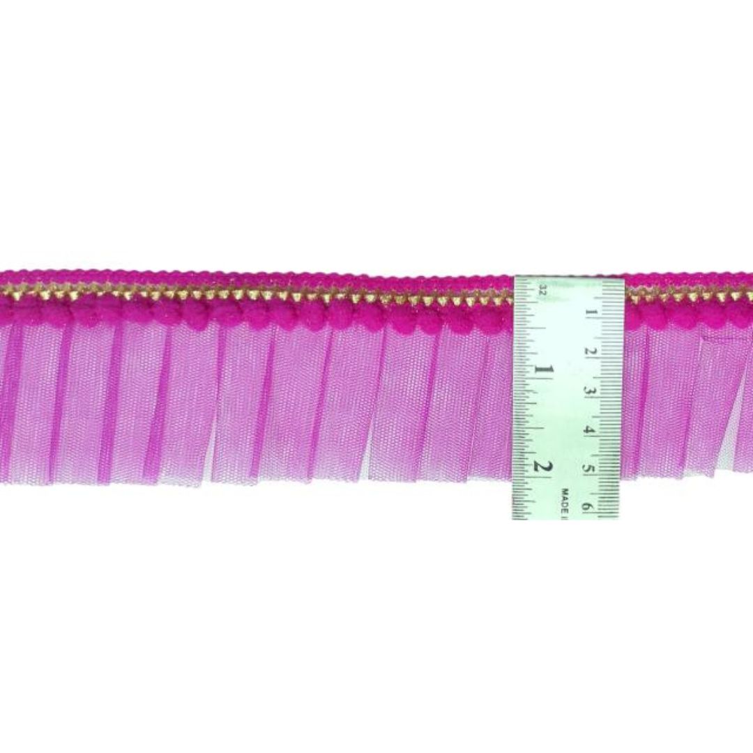 Pink fringe trim with gold accents and a ruler for scale on a white background