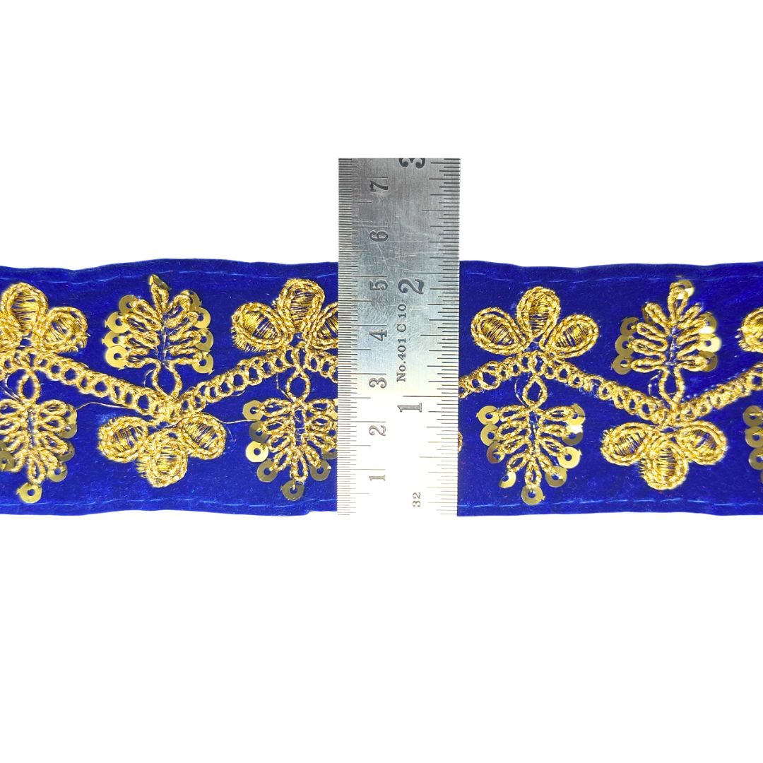 Decorative fabric trim with gold patterns on a blue background, measured against a ruler.