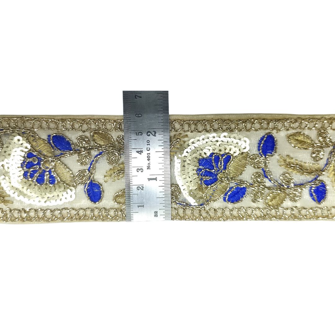 Decorative fabric trim with blue and gold floral patterns on a white background, measured against a ruler.
