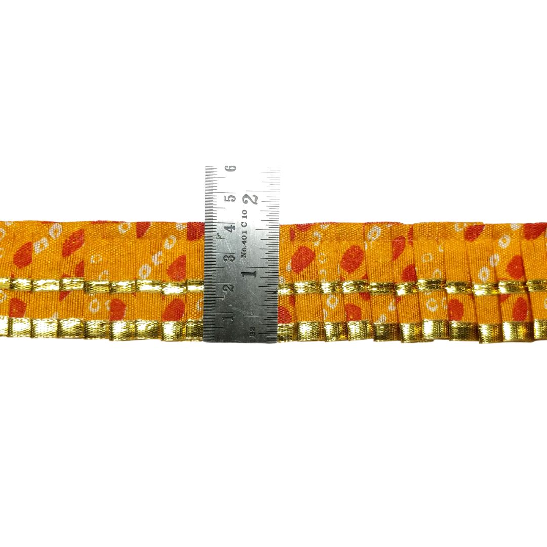 Yellow ribbon with red and gold pattern, measured against a ruler on a white background