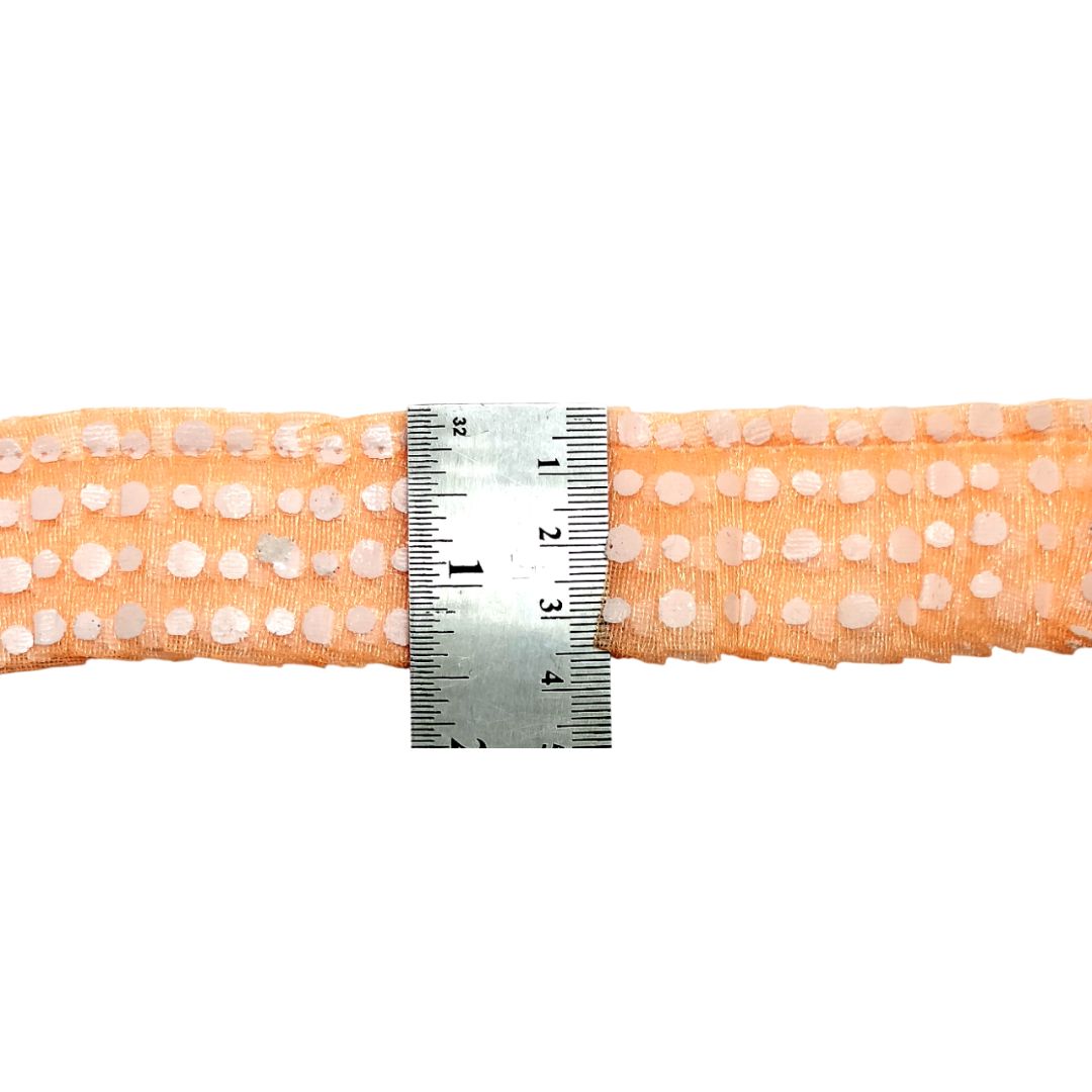 Peach-colored ribbon with white polka dots and a ruler for measurement on a white background