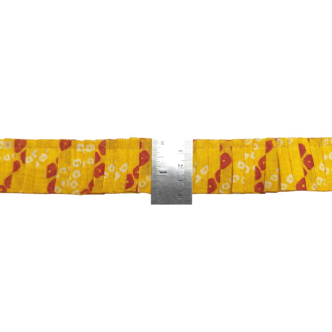 Yellow ribbon with red and white floral pattern and a metal ruler for scale on a white background